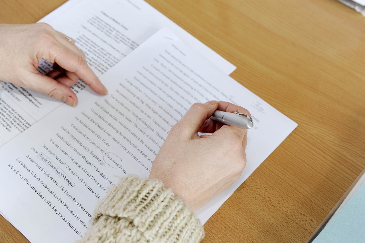Hands on documents, one with pen making corrections on the written page.